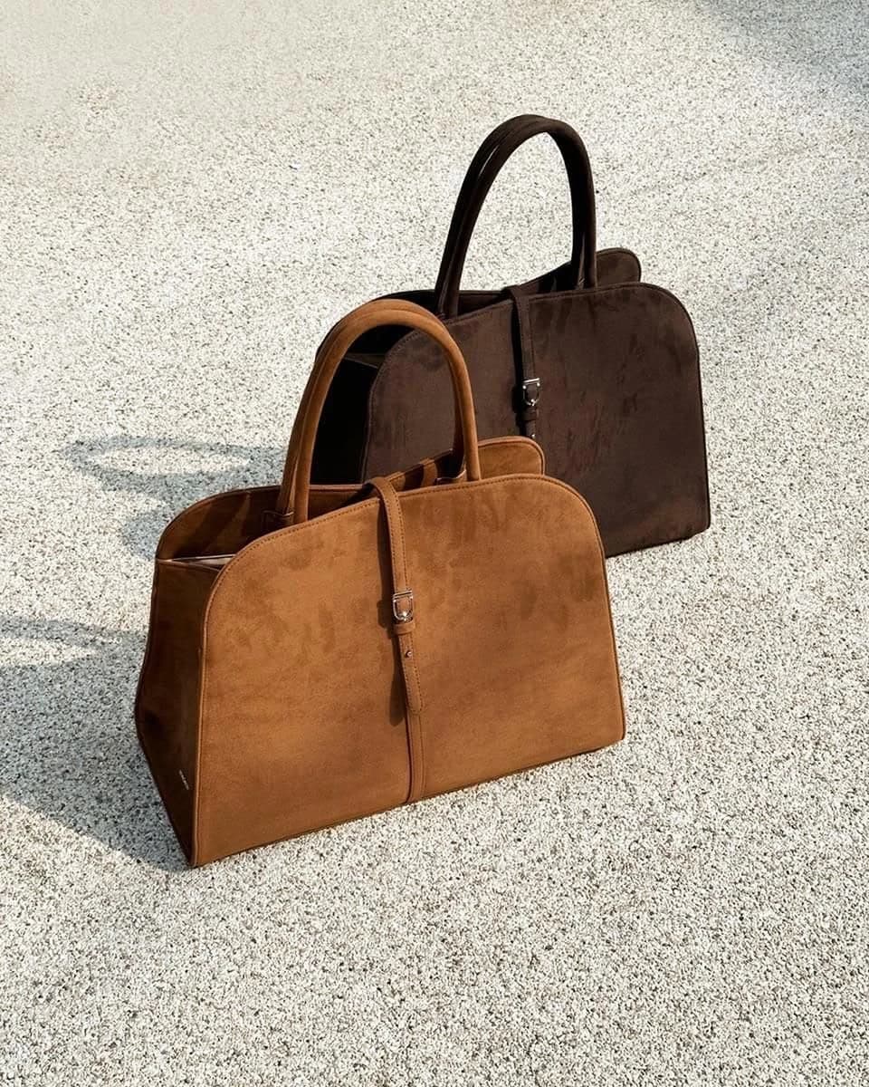ADUN Bag in Espresso suede, standing behind the Brown, both with two top handles and a buckled strap